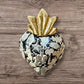 A Mexican Milagros heart in black with a gold flaming top, covered in antiqued charms. 