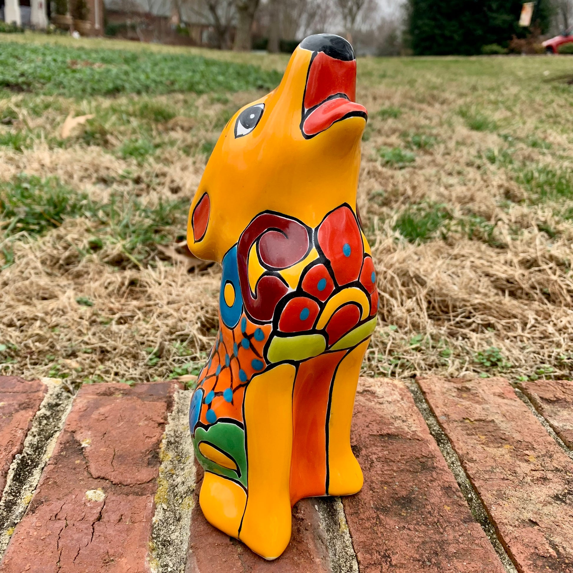 Colorful ceramic coyote figurine on a brick surface with grass in the background