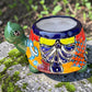 A colorful ceramic turtle-shaped planter with a green head and legs, decorated with vibrant hand-painted patterns in orange, yellow, blue, red, and white, sitting on a mossy stone outdoors.