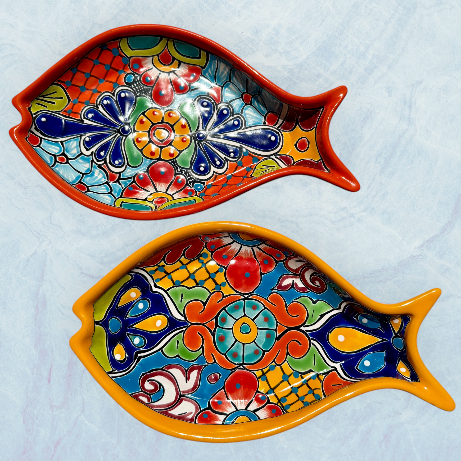 Two fish-shaped Talavera  serving dishes with colorful hand-painted floral and geometric patterns, displayed on a light blue textured background.