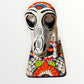 A ceramic Mexican-style skeleton dog figurine standing on a colorful floral base against a plain white background. Close up of front face.