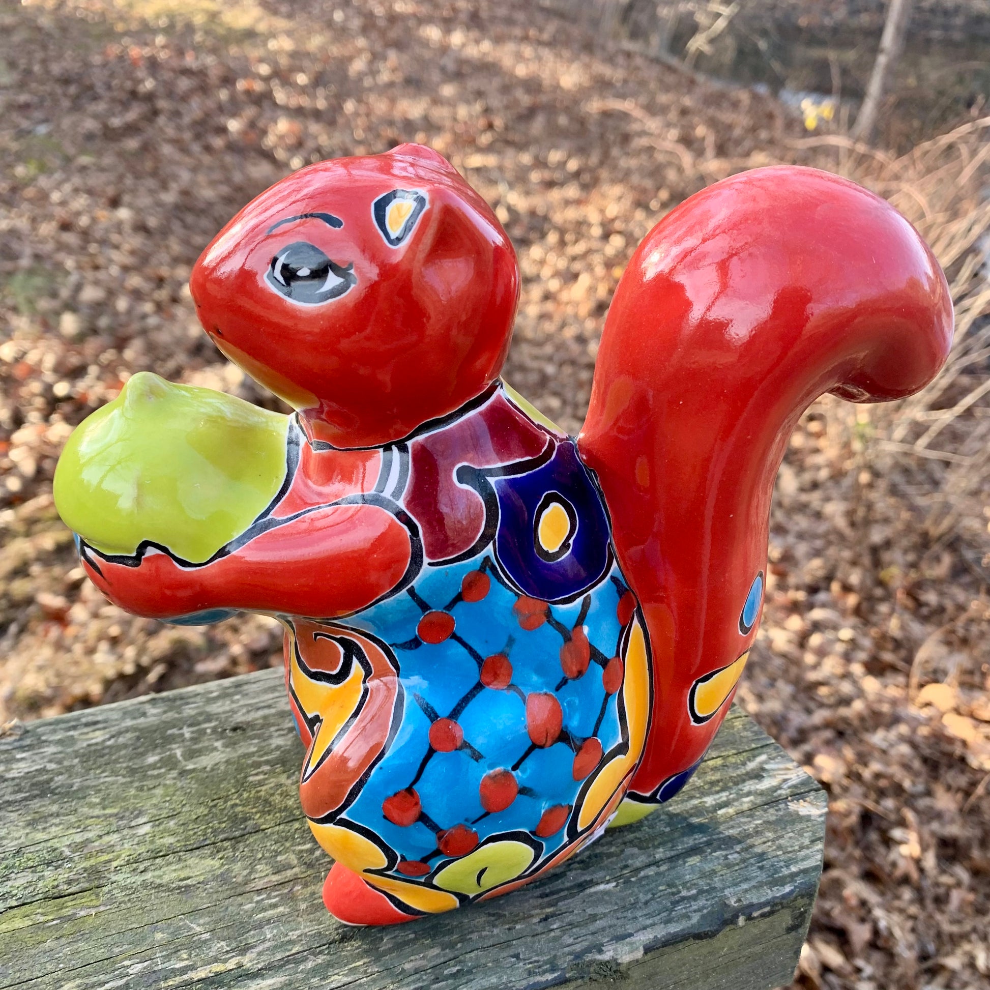 Colorful ceramic squirrel figurine holding an acorn on a wooden surface.