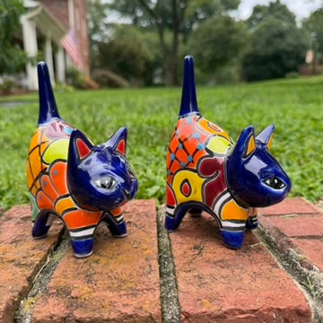 Two colorful hand-painted talavera ceramic cat figurines in cobalt blue with multi color designs standing on a brick path with a green lawn.