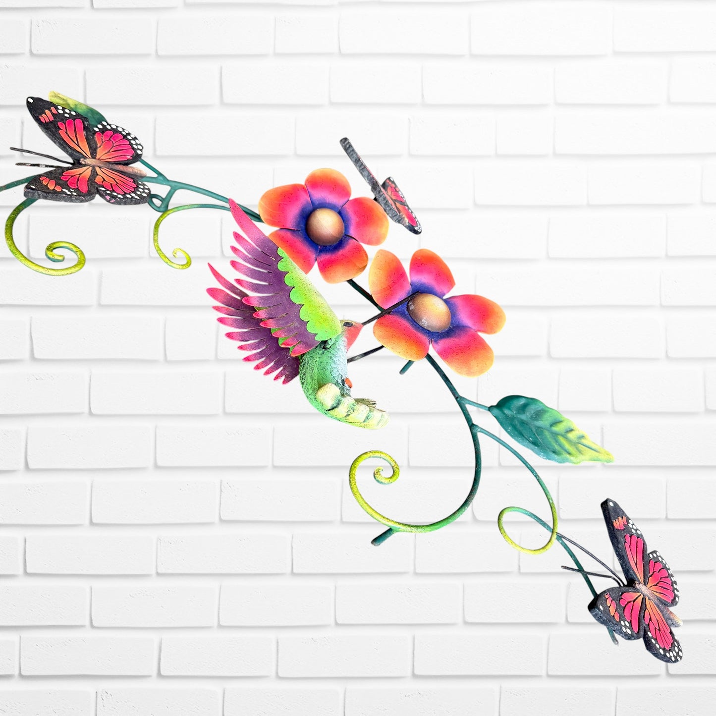 Decorative metal wall art with colorful flowers and butterflies on a white brick wall background three dimensional side view