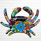 A colorful talavera crab wall art sculpture decorated with vibrant floral patterns, shown against a white brick wall background, top view of crab.