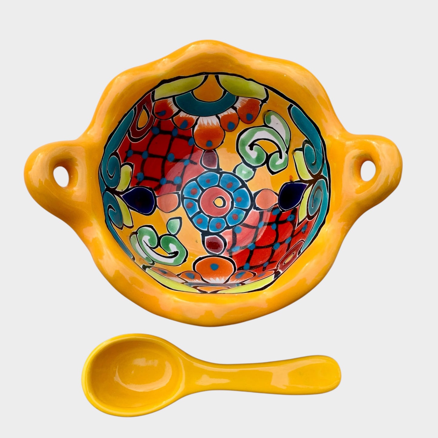 Colorful talavera salsa bowl with floral patterns and spoon on a white background