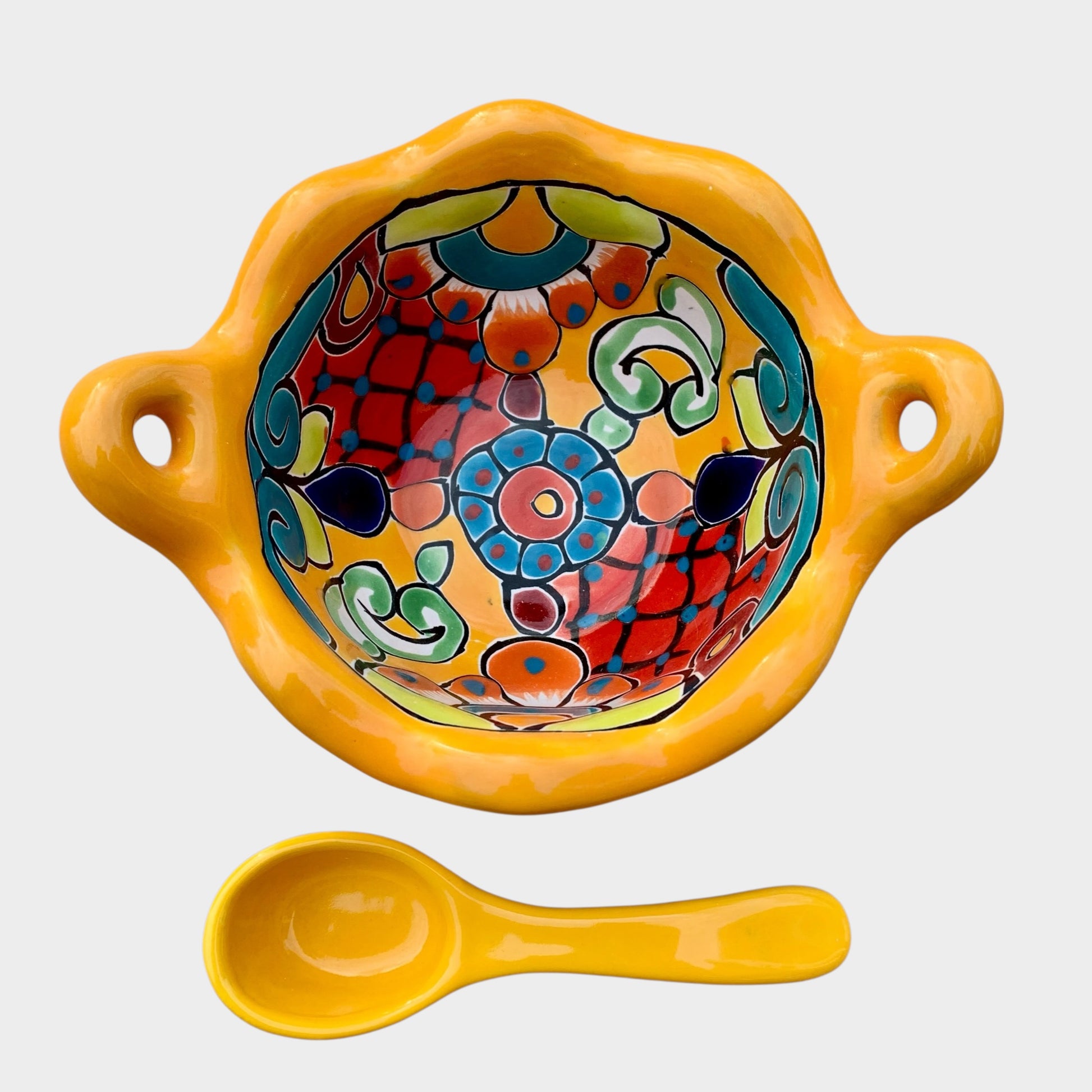 Colorful talavera salsa bowl with floral patterns and spoon on a white background