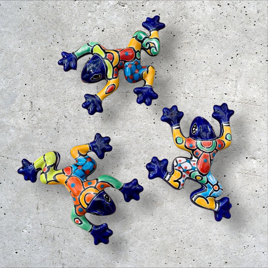 Three colorful talavera ceramic frogs on a textured gray surface