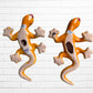 Two colorful hand-painted ceramic gecko wall sculptures in a vibrant Mexican folk art style, displayed side-by-side against a white brick wall back view showing hanging hole. 