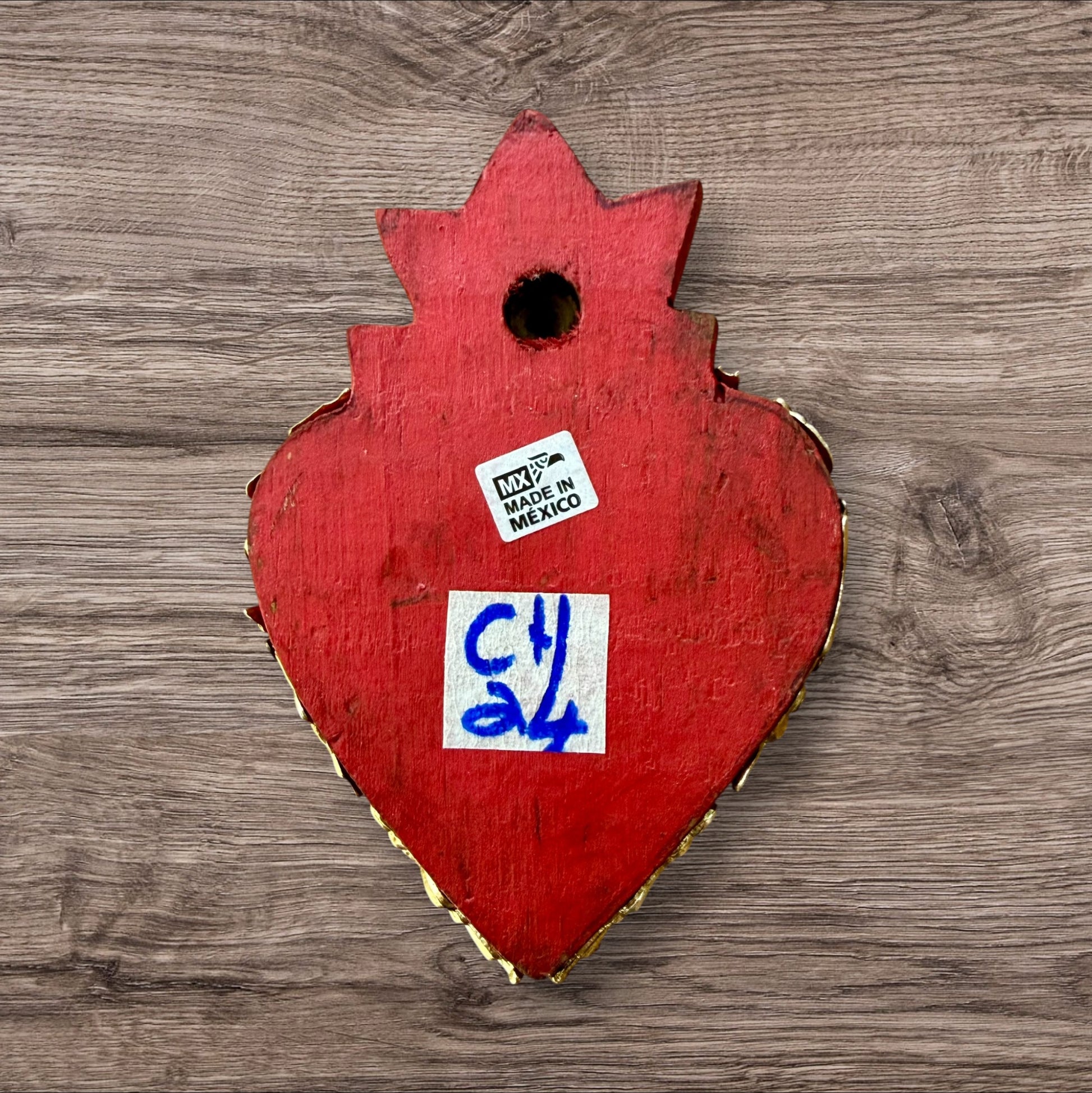 A Mexican Milagros heart in red with a gold flaming top, covered in silver charms, back view. 