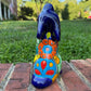 A colorful hand-painted Mexican Talavera Ceramic dog figurine sitting on a brick wall with a green grassy lawn and a house in the background back view.