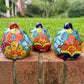 Three hand-painted Talavera ceramic jack-o'-lantern pumpkins in bright orange, yellow, red, green, and blue, sitting on a brick ledge with a blurred green lawn and house in the background, back view.