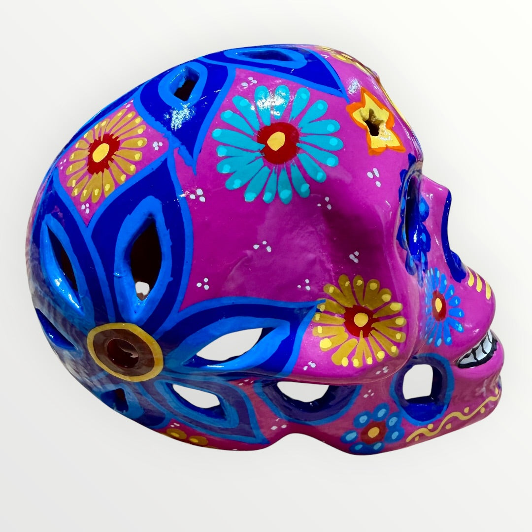 A hand-painted ceramic sugar skull mask in vibrant magenta pink, decorated with colorful floral and geometric patterns in blue, yellow, red, and white, set against a plain white background left side view.