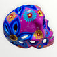 A hand-painted ceramic sugar skull mask in vibrant magenta pink, decorated with colorful floral and geometric patterns in blue, yellow, red, and white, set against a plain white background left side view.