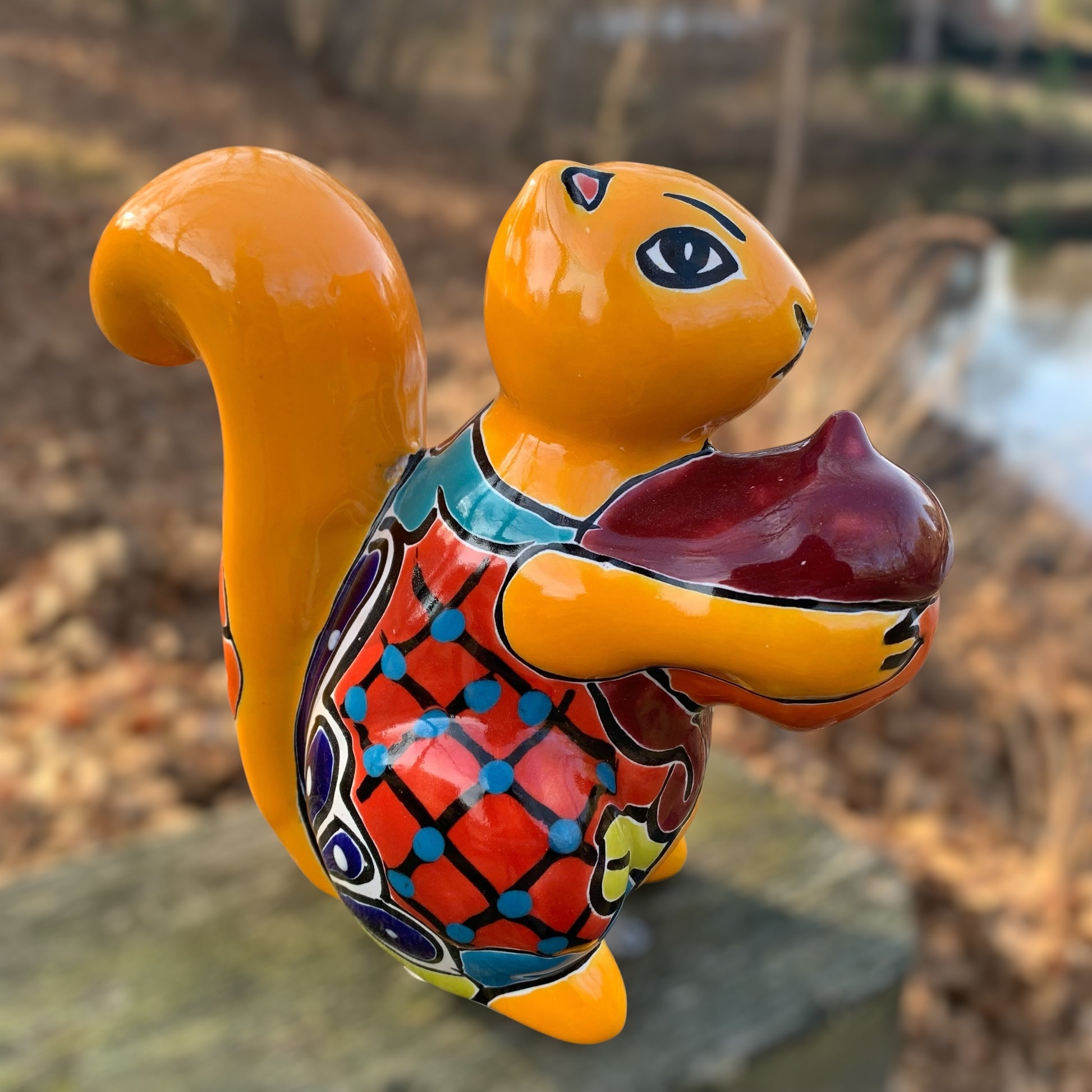 Colorful ceramic squirrel figurine with a red nut on a natural background in yellow