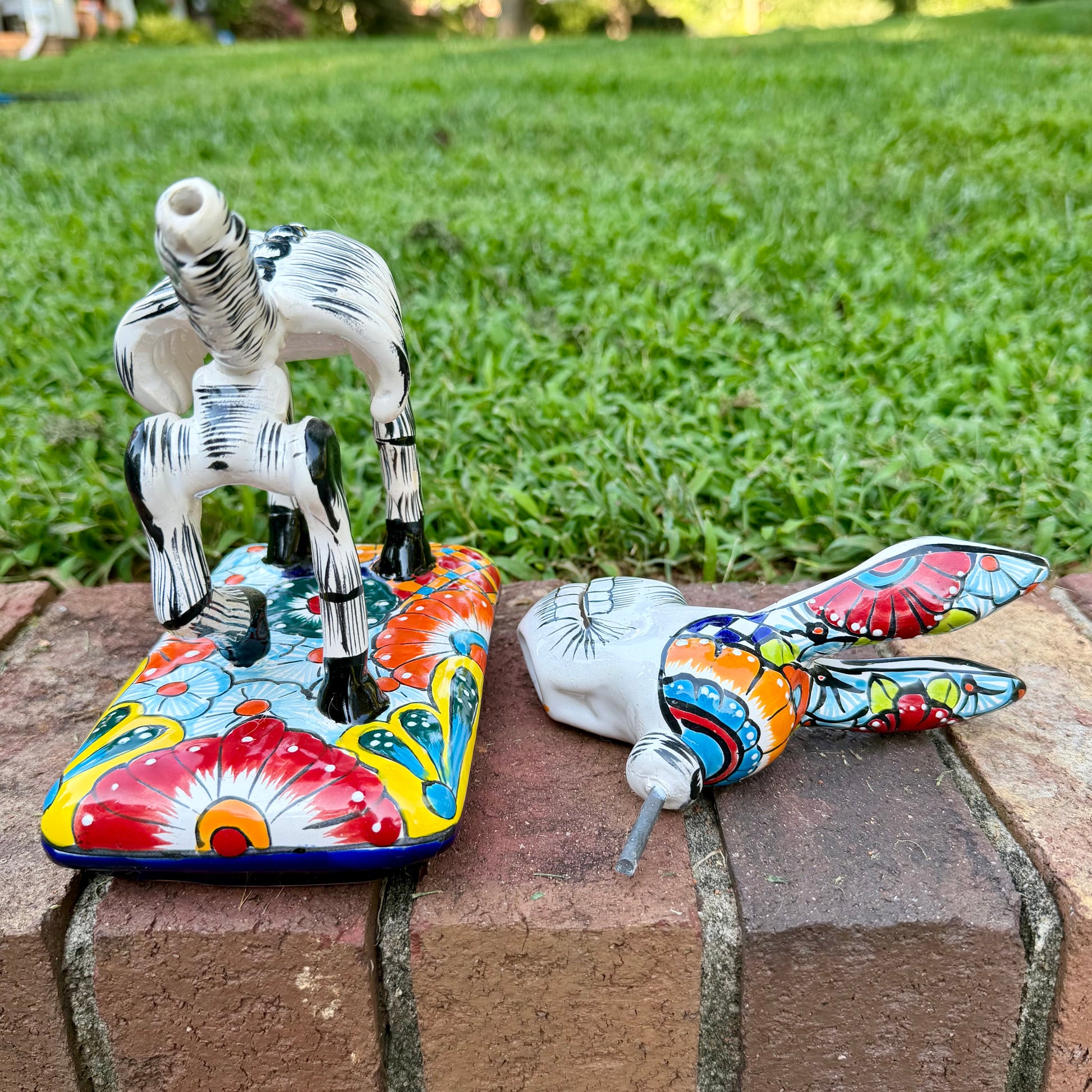A colorful hand-painted Talavera Catrina donkey figurine, standing on a colorful floral base in an outdoor backyard setting, View of base with head off.