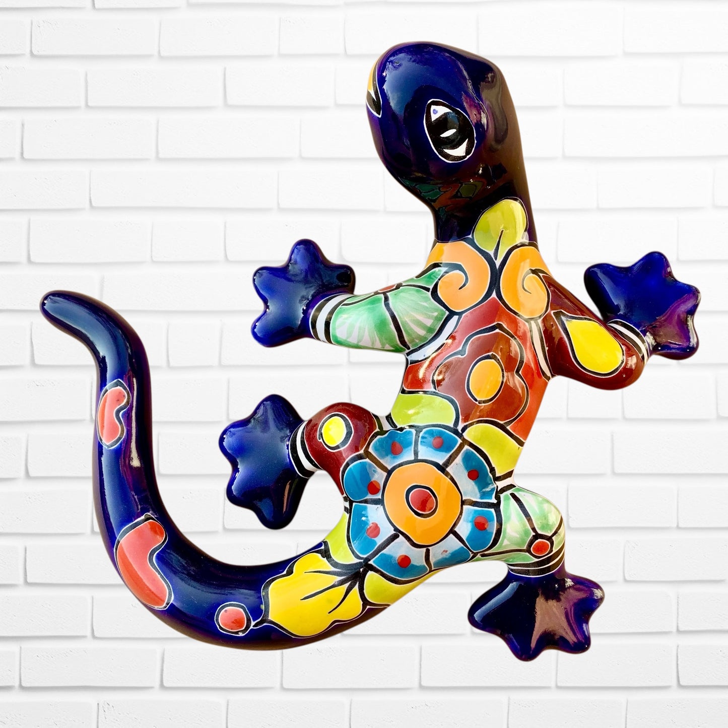 Colorful blue ceramic lizard wall art against a white brick wall background 