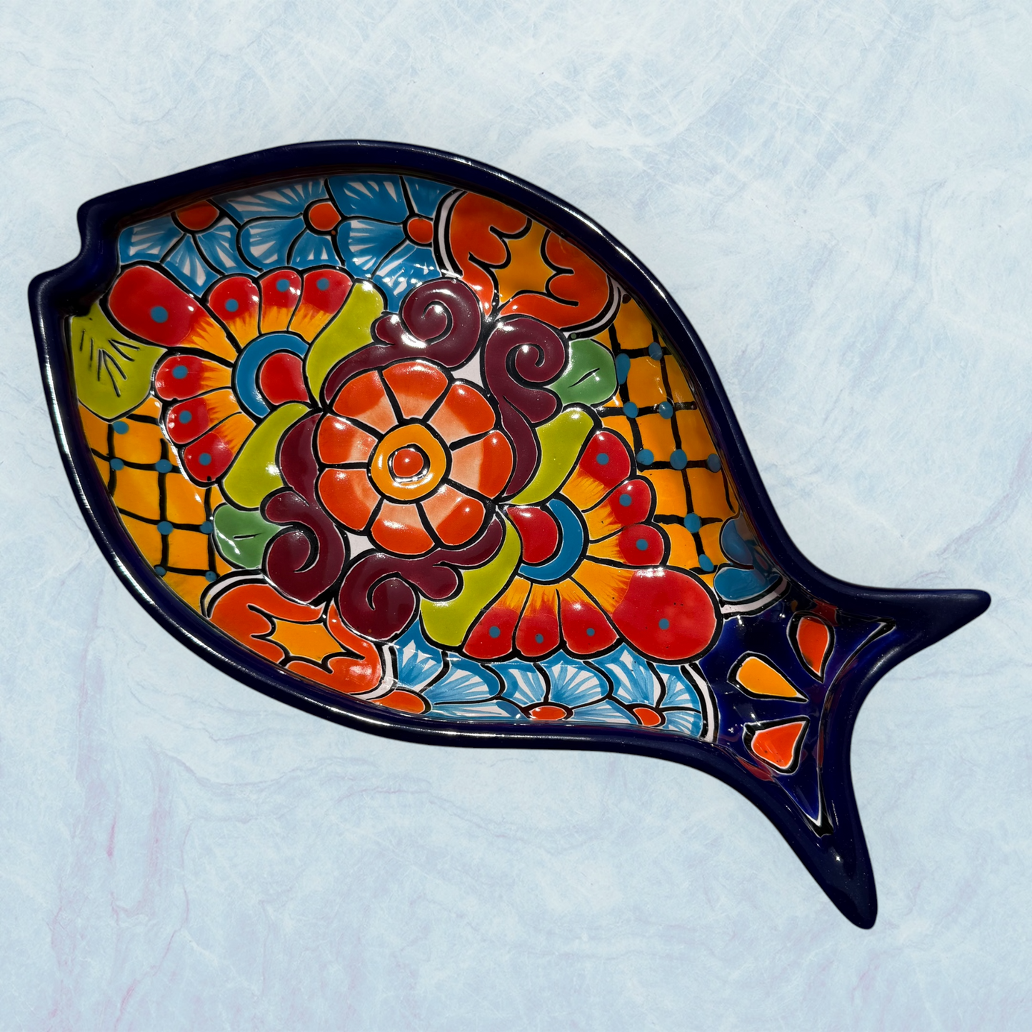 decorative blue fish-shaped ceramic plates with vibrant hand-painted floral and geometric patterns in red, orange, yellow, green, blue, and purple, set against a light blue background.
