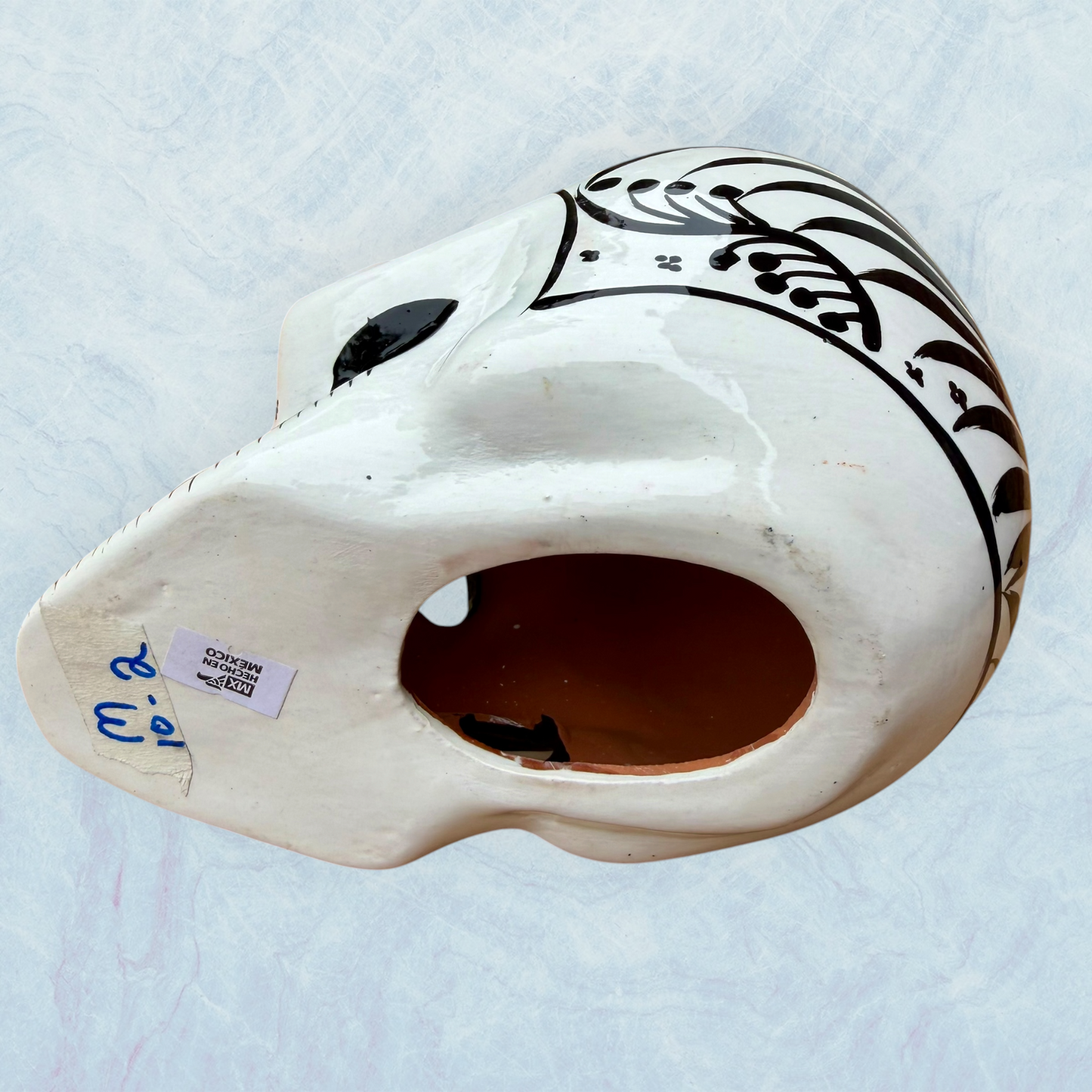 A decorative skull sculpture with intricate black sugar skull style patterns painted on an off-white base, set against a light blue textured background, bottom view.