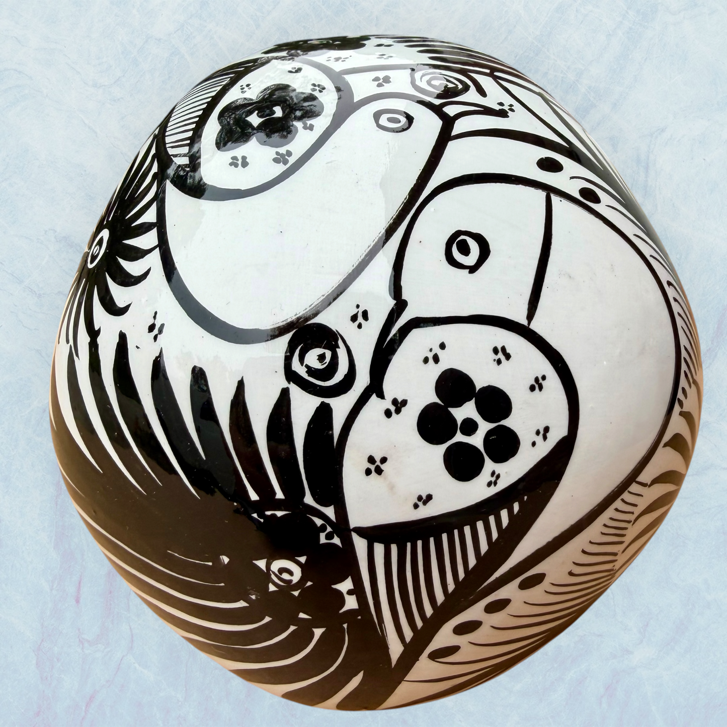 A decorative skull sculpture with intricate black sugar skull style patterns painted on an off-white base, set against a light blue textured background, back view.