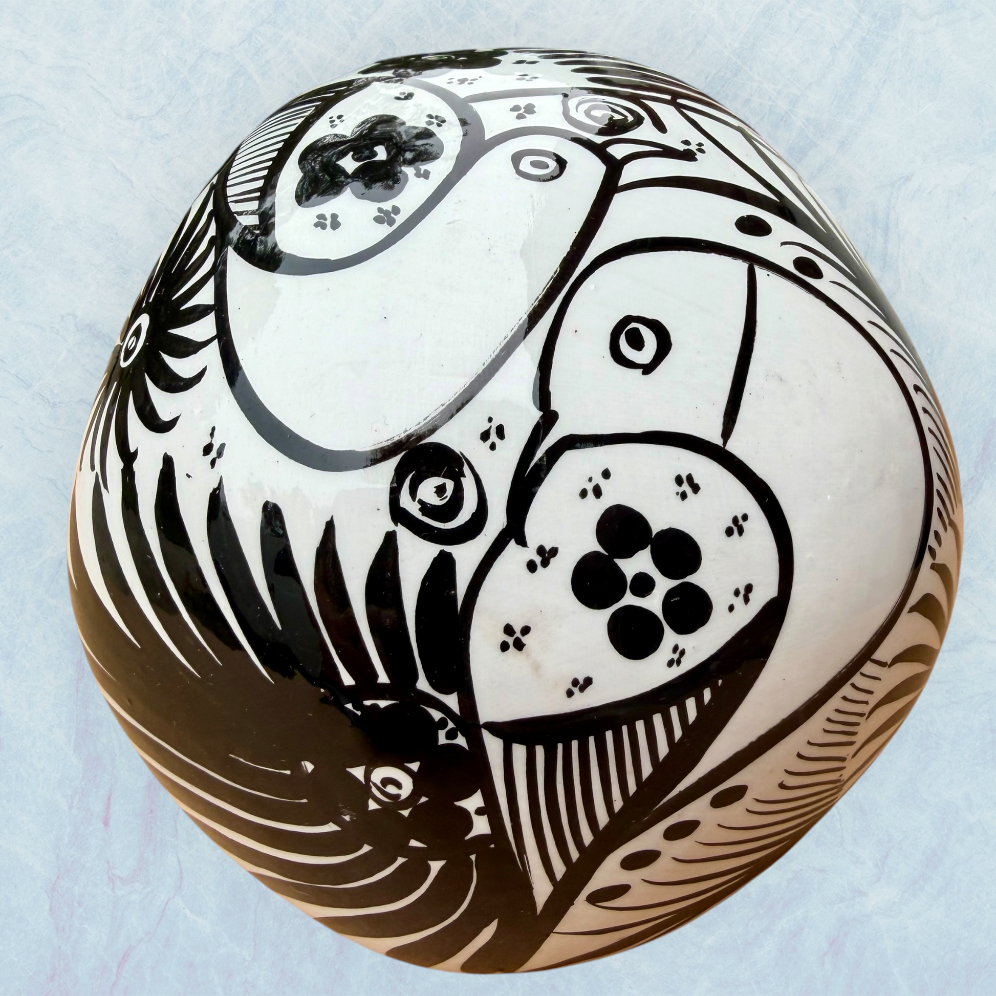 A decorative skull sculpture with intricate black sugar skull style patterns painted on an off-white base, set against a light blue textured background, back view.