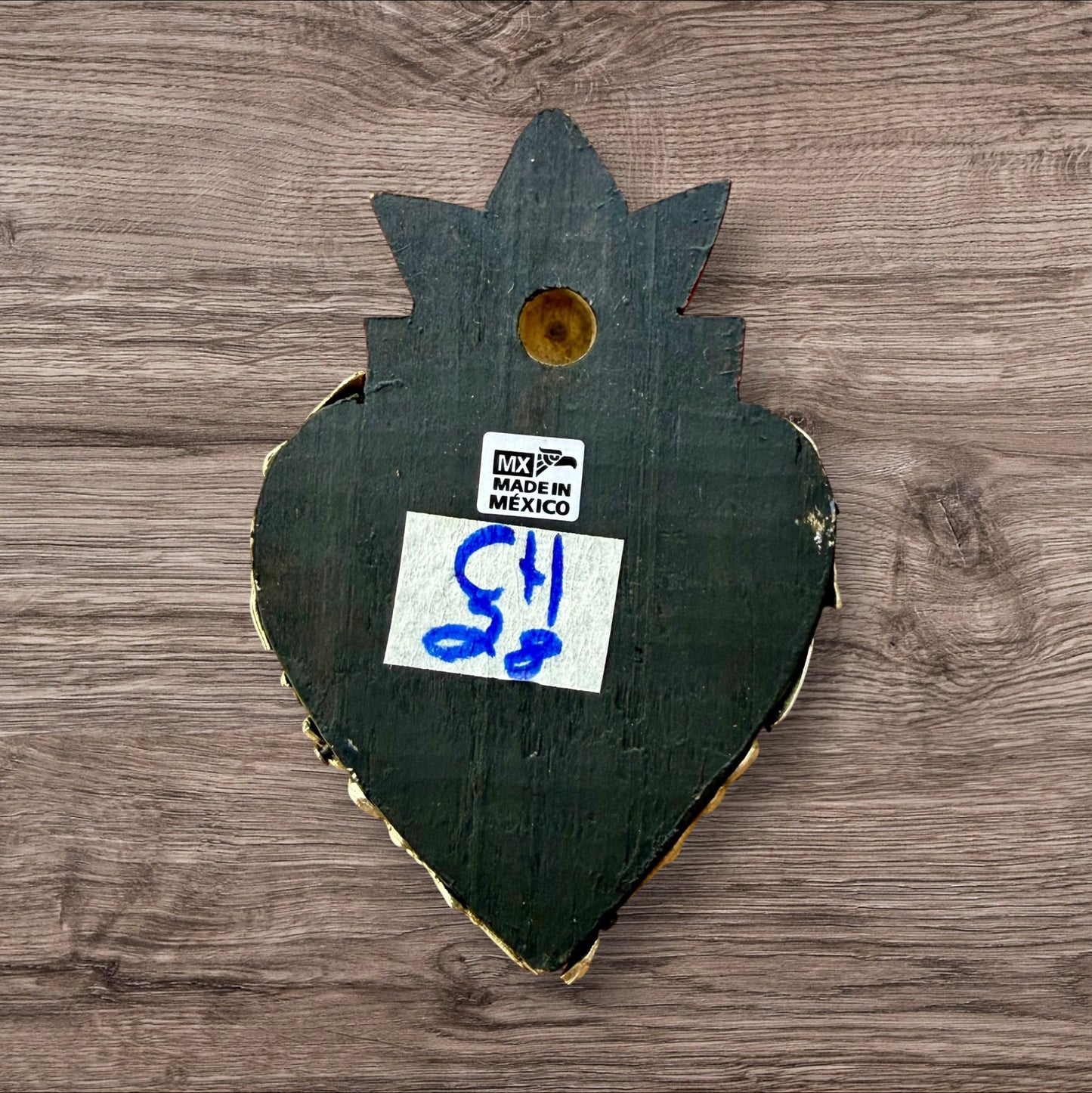 A Mexican Milagros heart in black with a gold flaming red top, covered in golden charms, back view. 
