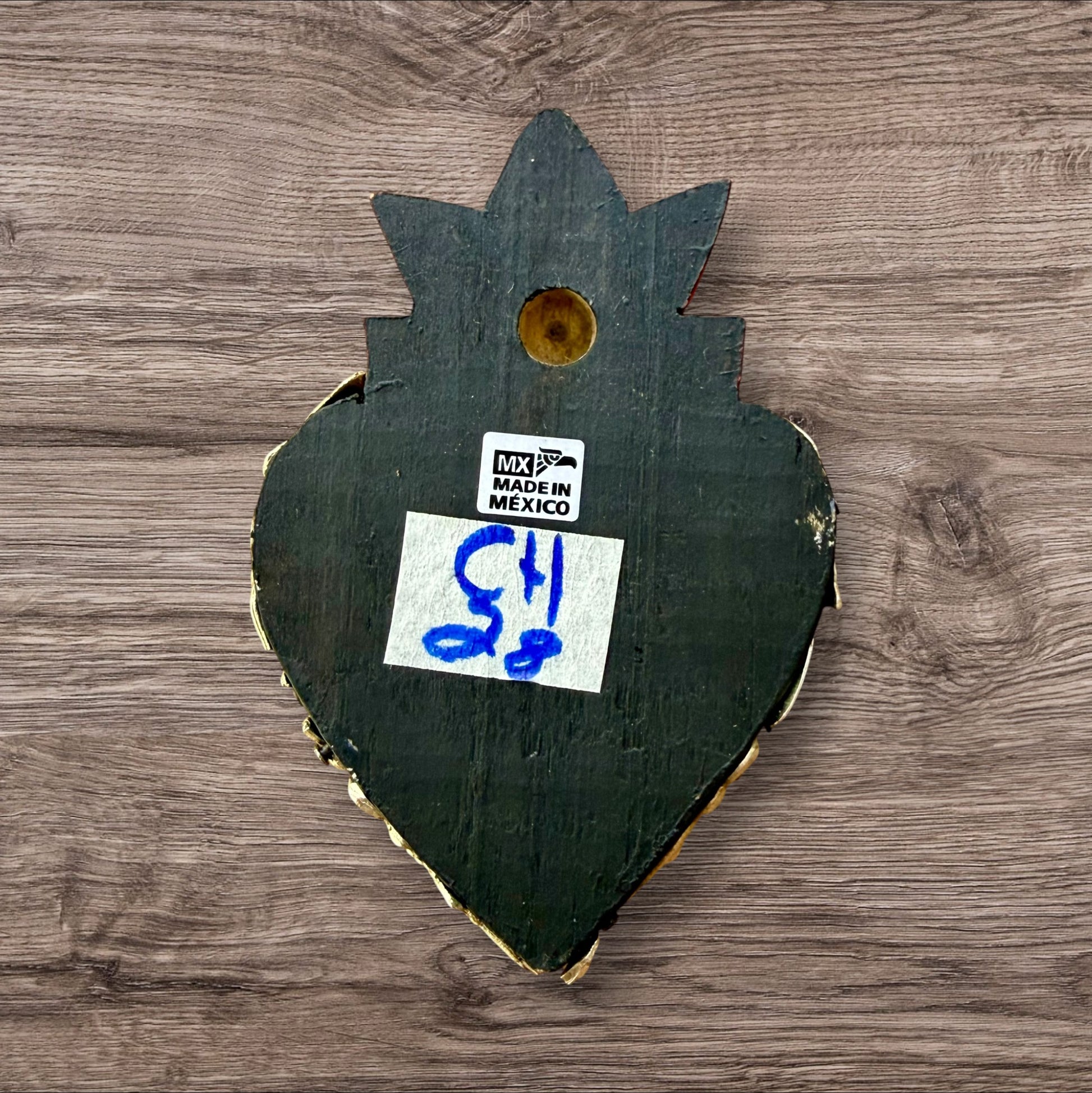 A Mexican Milagros heart in black with a gold flaming red top, covered in golden charms, back view. 