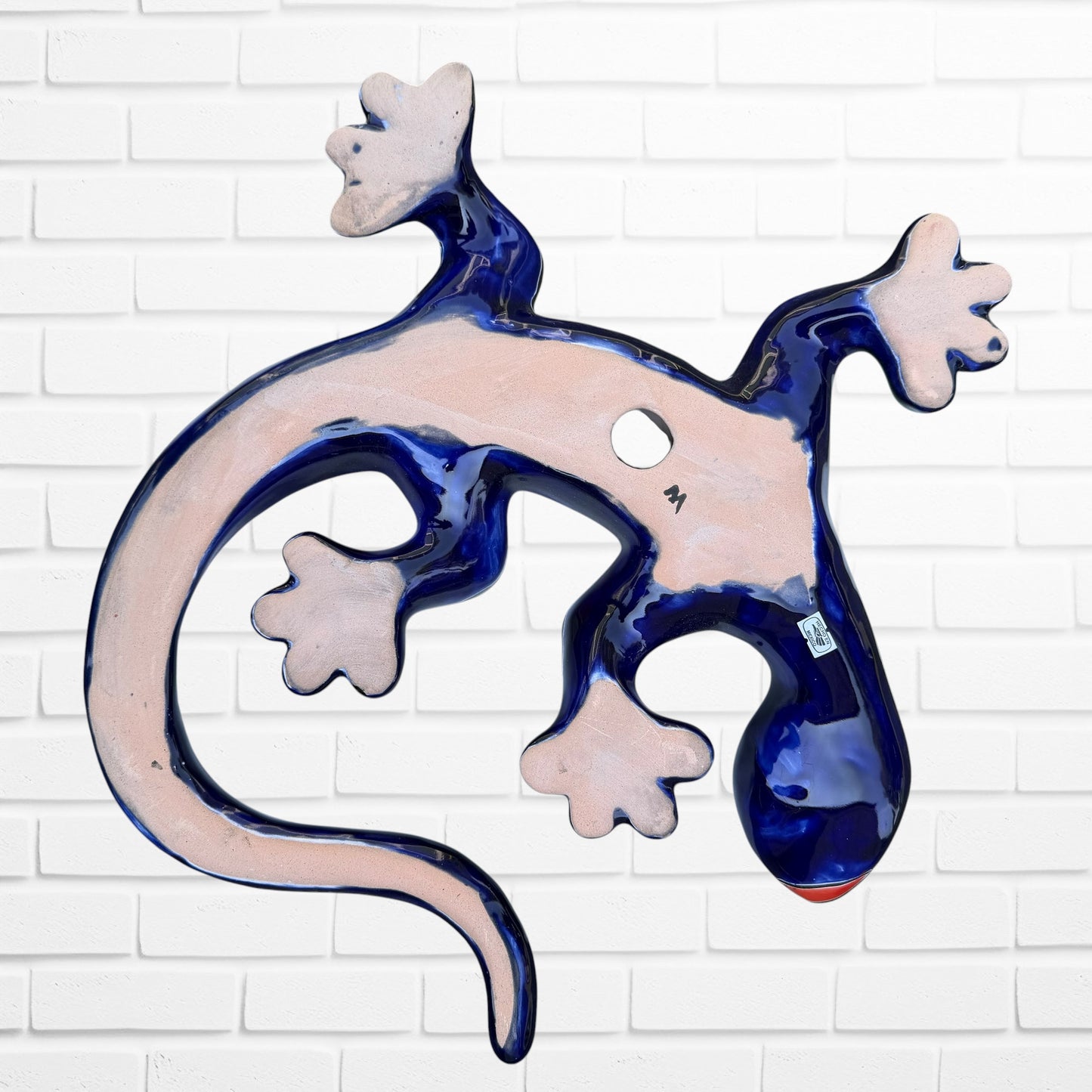 A colorful Talavera ceramic wall sculpture of a salamander, featuring a glossy finish and intricate hand-painted patterns in blue, orange, red, yellow, and white, mounted against a white brick wall, fairview Showing hole for wall mounting.