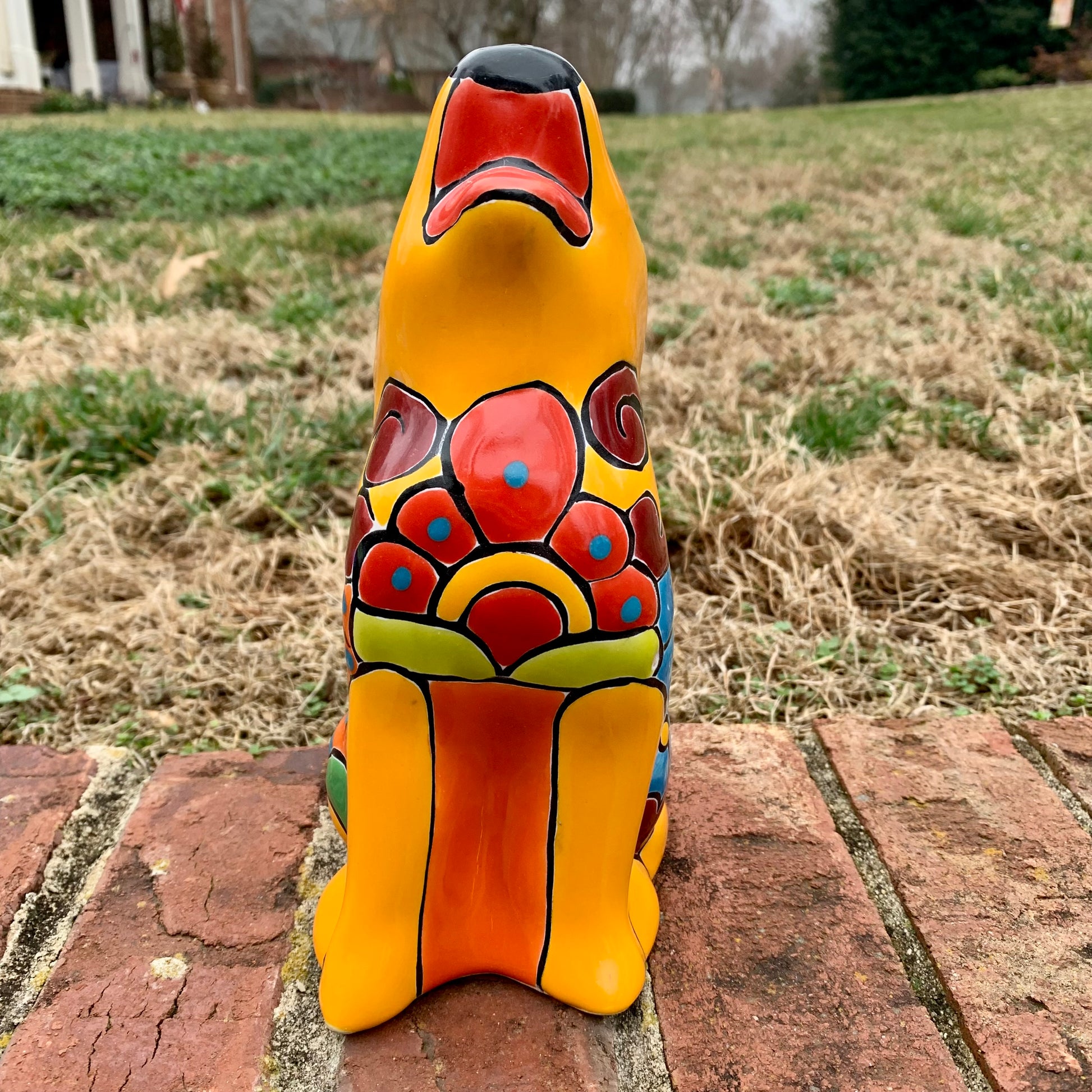 Colorful ceramic coyote sculpture on a brick surface with grass in the background