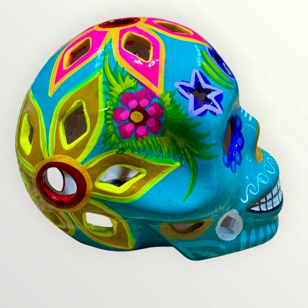 A decorative sugar skull painted in bright turquoise blue with colorful floral and geometric patterns in pink, yellow, green, purple, and white, shown against a plain light background left side view

