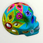 A decorative sugar skull painted in bright turquoise blue with colorful floral and geometric patterns in pink, yellow, green, purple, and white, shown against a plain light background left side view
