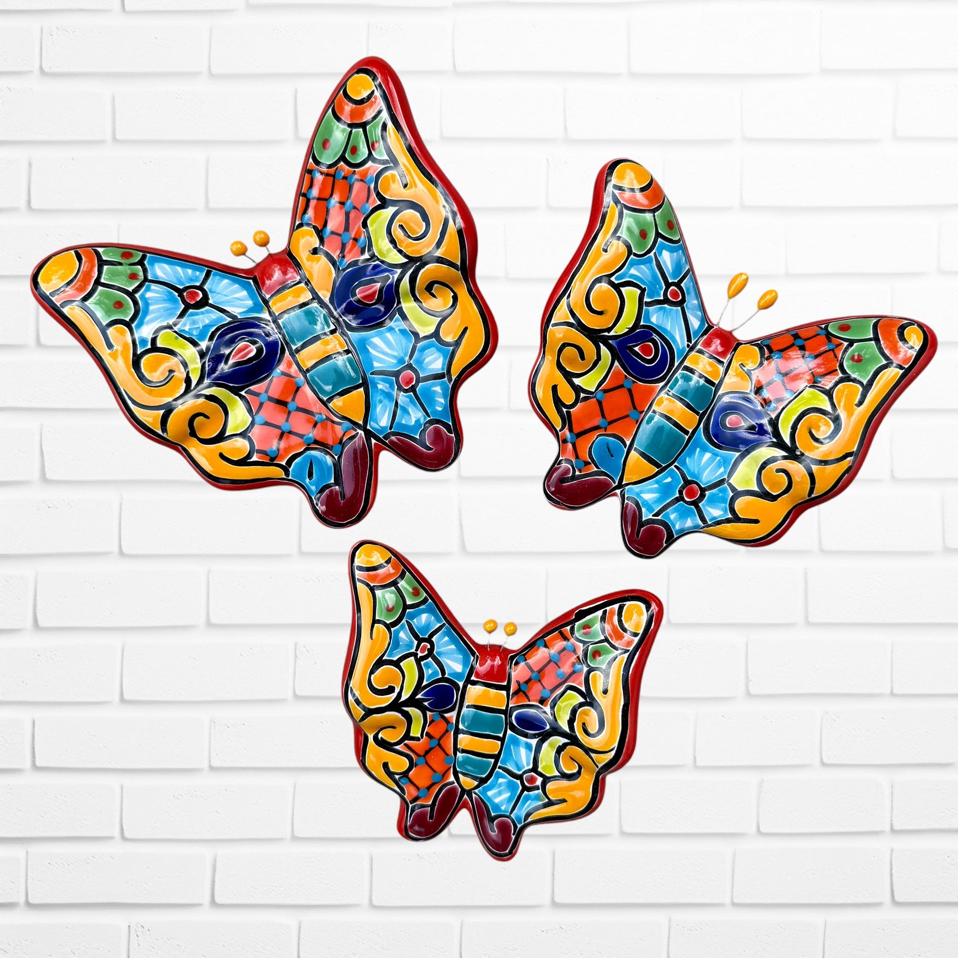 Three colorful talaver butterfly wall art pieces with a traditional style pattern, displayed against a white brick wall.