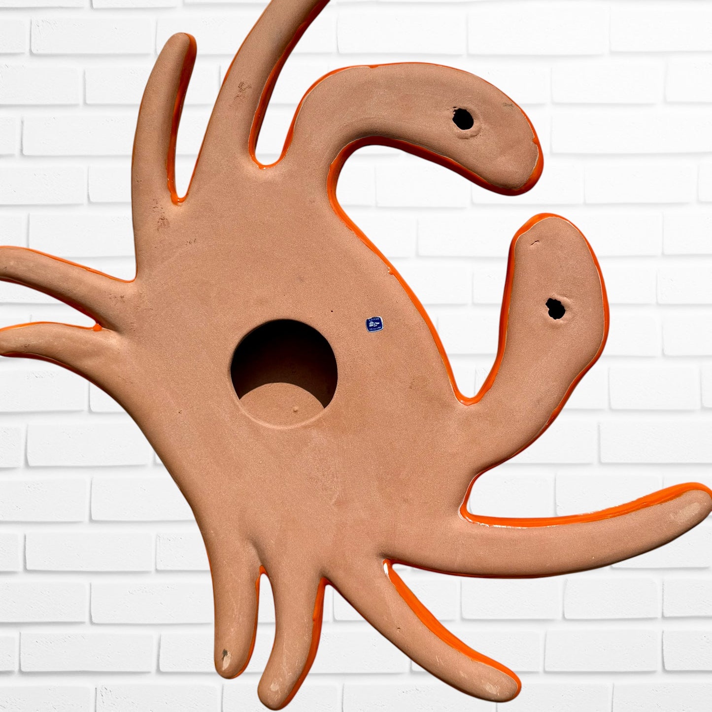 A colorful multicolor hand-painted wall art sculpture of a crab, decorated with vibrant floral patterns, shown against a white brick wall background, bottom.