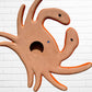 A colorful multicolor hand-painted wall art sculpture of a crab, decorated with vibrant floral patterns, shown against a white brick wall background, bottom.