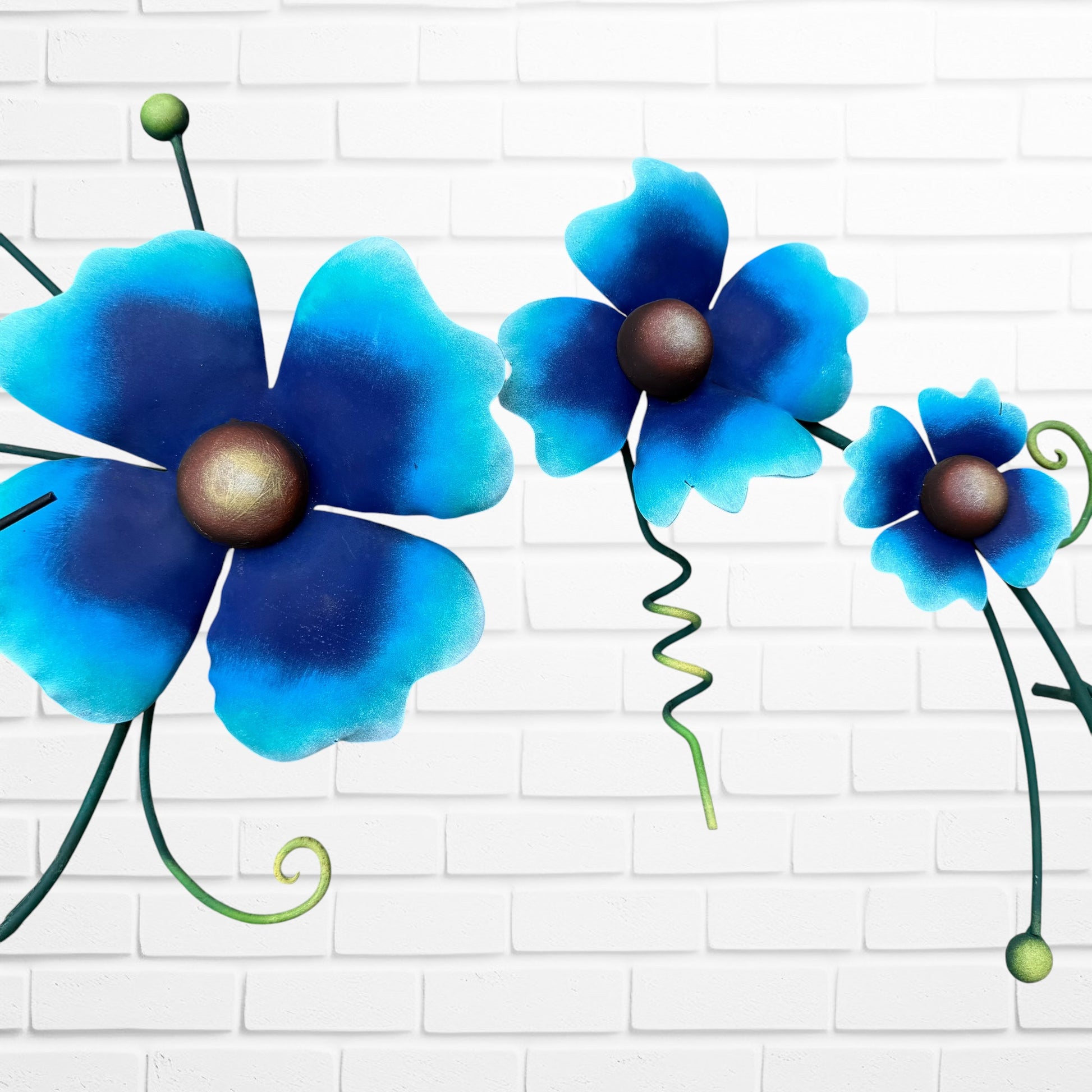 Decorative metal wall art with three blue flowers and a colorful hummingbird on a white brick background floral close up