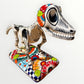 A ceramic Mexican-style skeleton dog figurine standing on a colorful floral base against a plain white background.