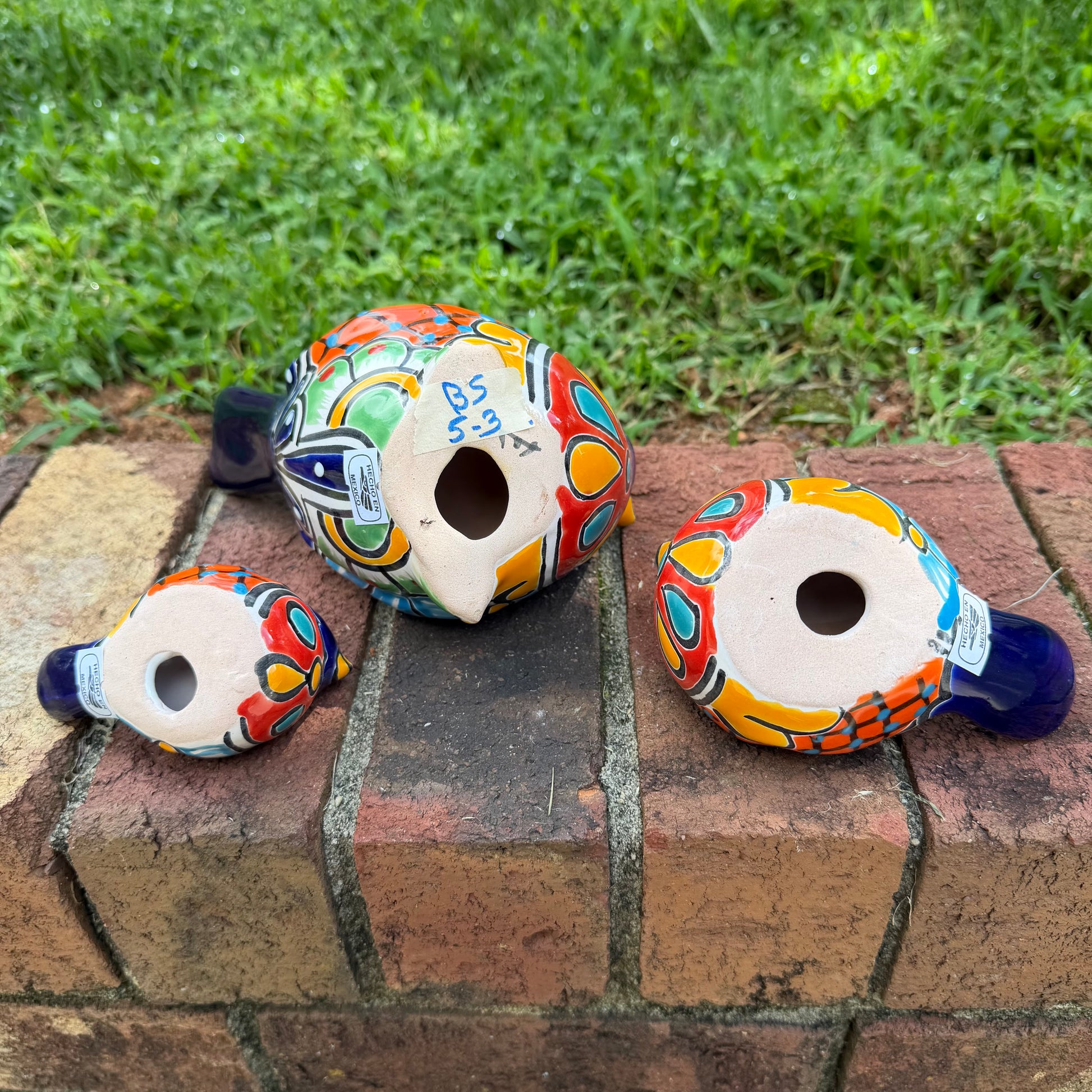 Three hand-painted ceramic bird figurines in different sizes, decorated with a vibrant Mexican Talavera style pattern of blue, red, yellow, and white, bottom view of birds.
