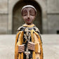 A carved milagros religious figurine of  Saint Martin in ornate black and gold vestments with silver cross details, photographed outdoors in front of a blurred stone archway.