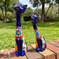 Two colorful glazed ceramic cat figurines sitting on a brick path in a grassy outdoor garden setting.