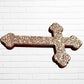 Decorative Milagros wood cross with many charms “miracles” on a white brick wall background Right side