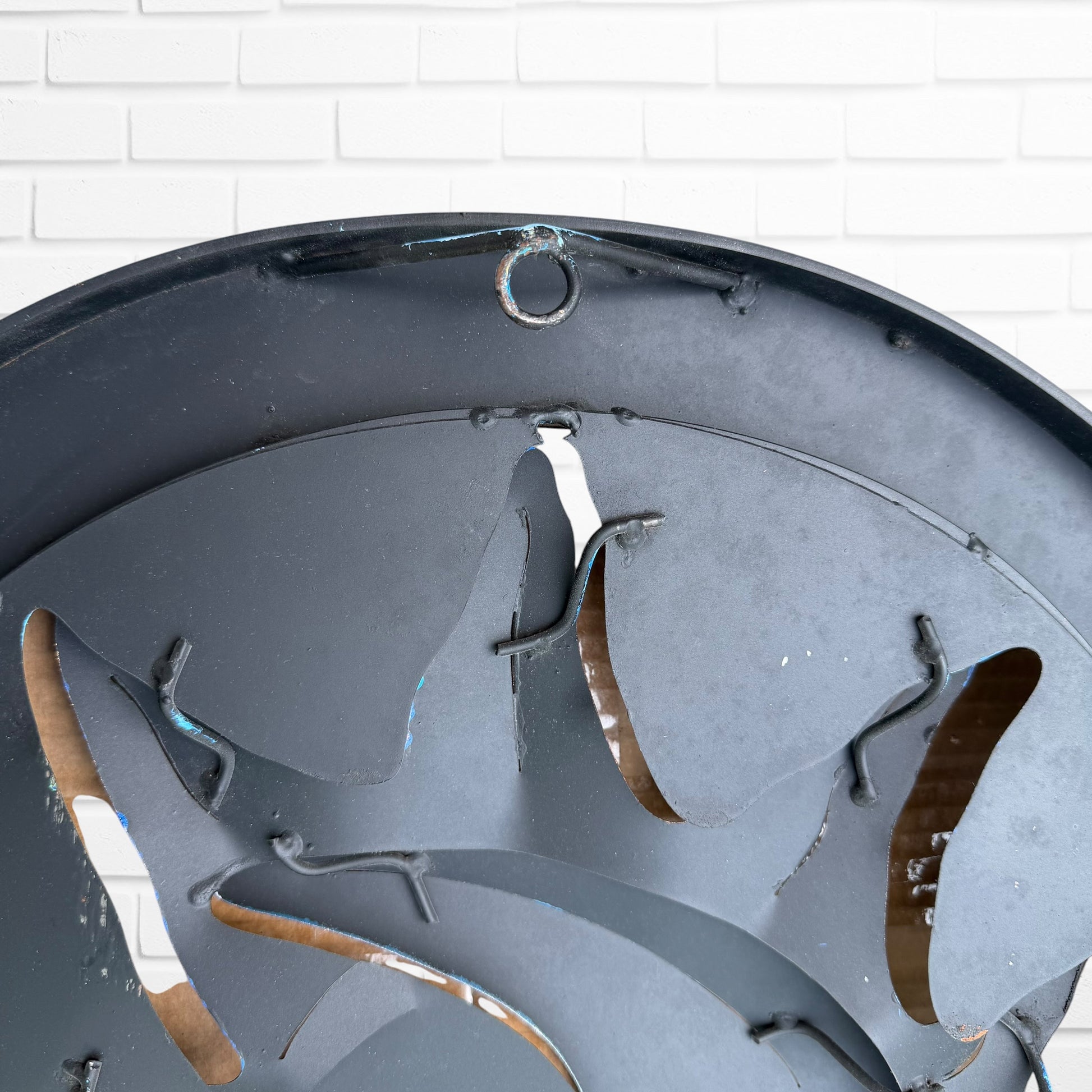 Decorative wall art of a sun and moon face with a metal frame on a white brick wall. Designed by artist Andres Martin hanging loop
