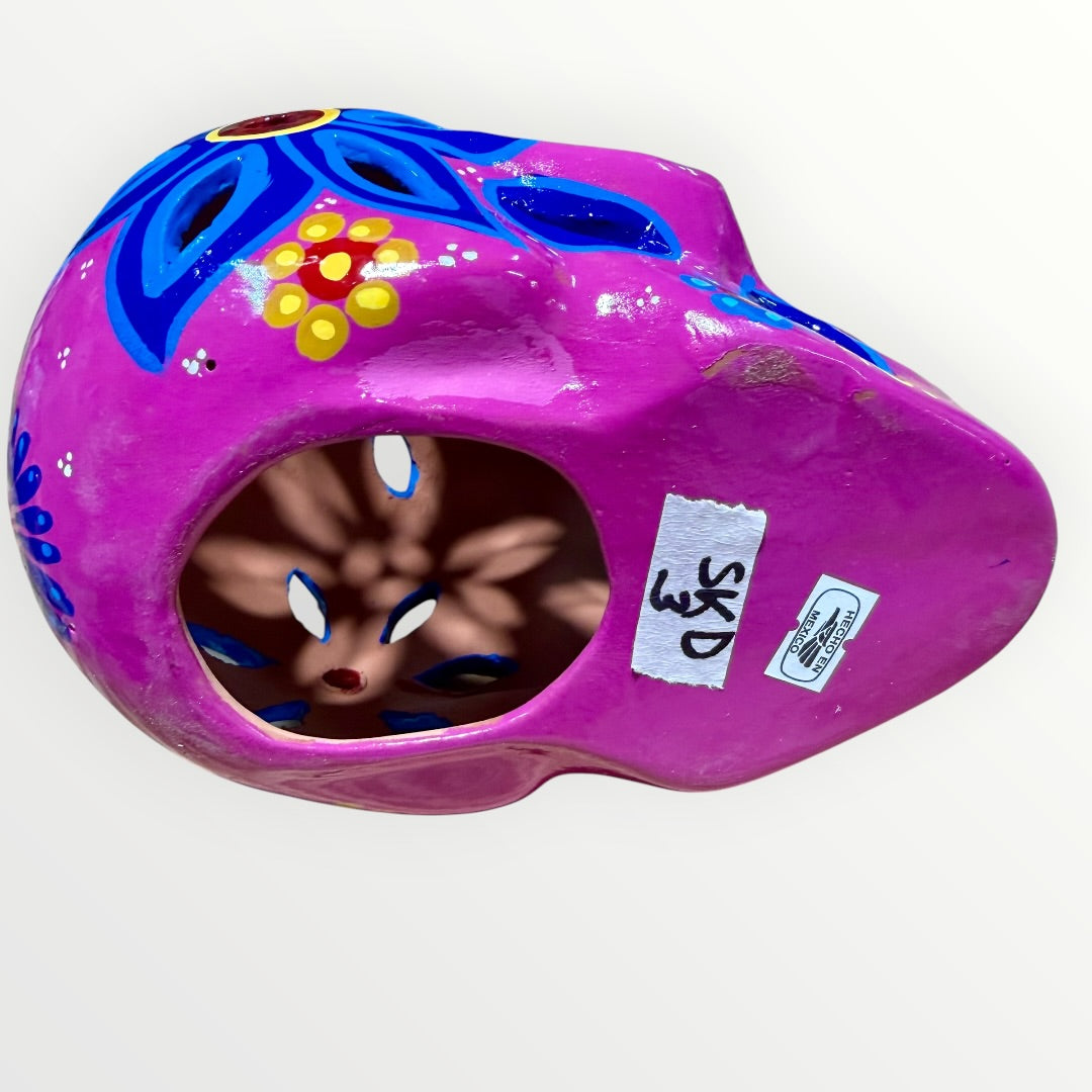 A hand-painted ceramic sugar skull mask in vibrant magenta pink, decorated with colorful floral and geometric patterns in blue, yellow, red, and white, set against a plain white background bottom of skull opening.