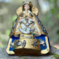 Angled view of Milagros Virgin Mary Salud showing her halo, crown and charms on her blue robe.