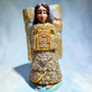 Milagros wooden guardian angel figurine wearing a yellow robe with gold and silver metallic details, standing on a light blue textured background.
