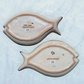 Two decorative fish-shaped talavera serving plates with colorful hand-painted floral and geometric patterns, displayed on a light blue background, back view.