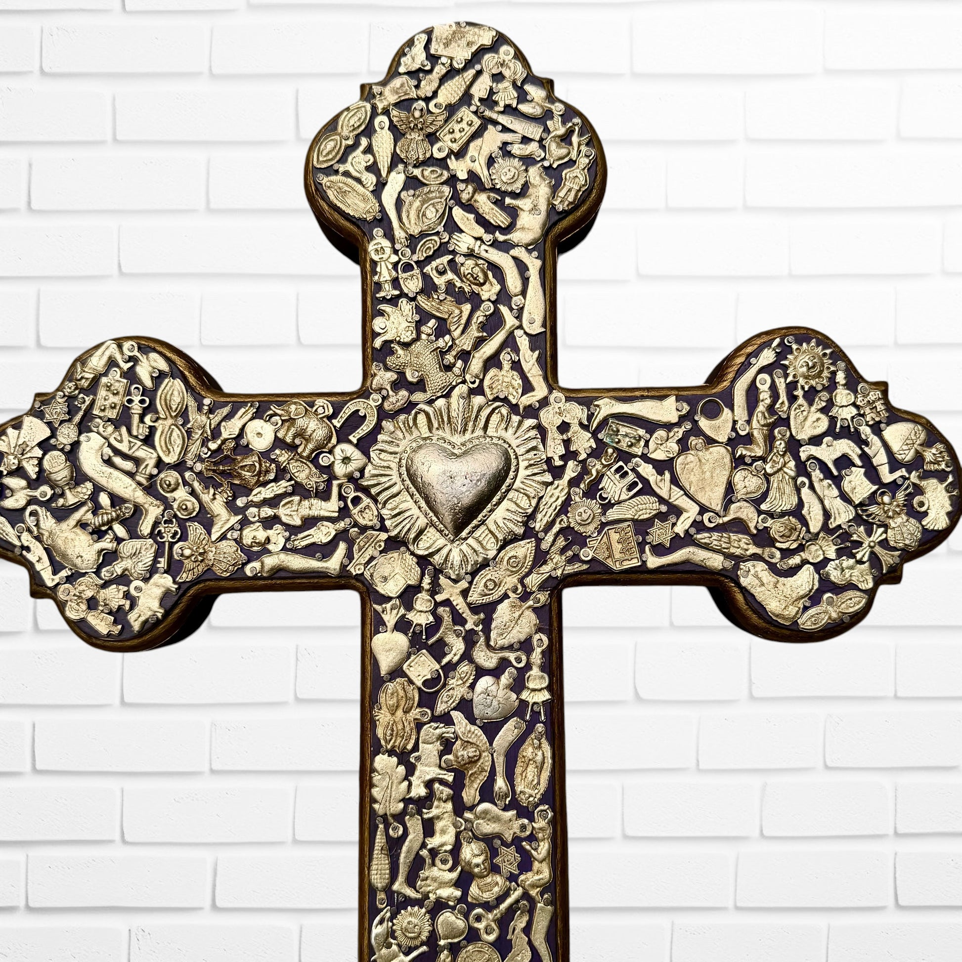 Decorative Milagros wood cross with many charms “miracles” on a white brick wall background Center heart 