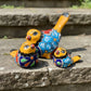 Three hand-painted ceramic bird figurines in yellow, decorated with intricate blue, black, red, green, and orange floral patterns, arranged on a rustic wooden surface.