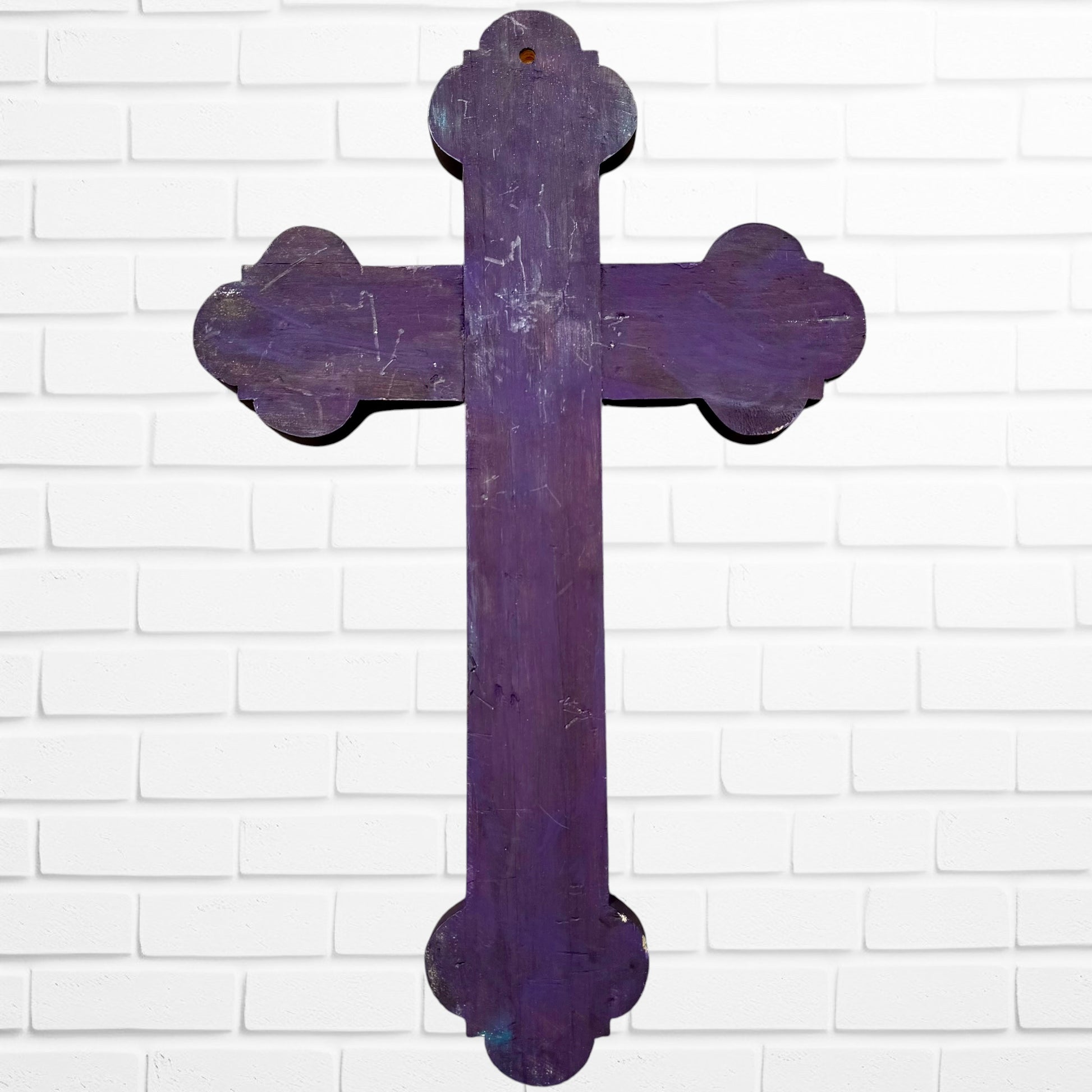 Decorative Milagros wood cross with many charms “miracles” on a white brick wall background Back