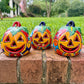 Three hand-painted Talavera ceramic jack-o'-lantern pumpkins in bright orange, yellow, red, green, and blue, sitting on a brick ledge with a blurred green lawn and house in the background.