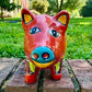 A colorful hand-painted red Talavera ceramic pig figurine standing on a brick surface with a blurred green lawn and trees in the background face close up